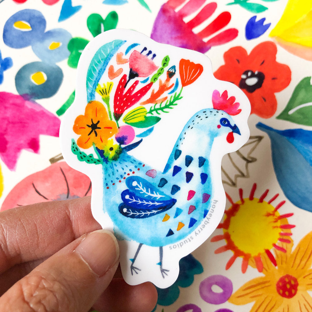 Colorful watercolor rooster sticker with floral patterns held by hand, surrounded by vibrant abstract shapes and flowers on white background