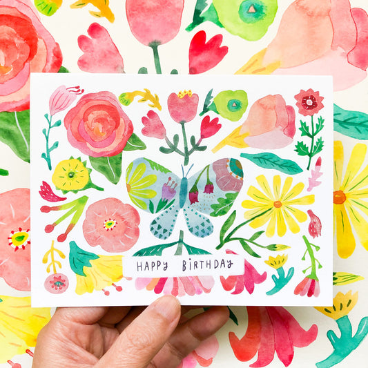 Colorful watercolor birthday card featuring vibrant floral design with roses, tulips, daisies, and a central butterfly. Text reads "Happy Birthday" surrounded by cheerful pink, yellow, and green botanical elements.