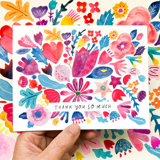 Colorful watercolor floral thank you card with vibrant pink, red, purple, and blue flowers, leaves, and hearts surrounding "Thank you so much" text, held by a hand against a matching floral background