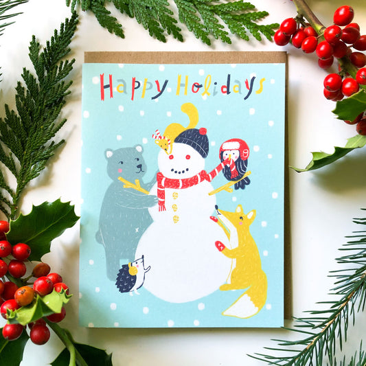 Festive holiday card featuring a cheerful snowman with animal friends, surrounded by greenery and red berries, on a light blue background with 'Happy Holidays' text