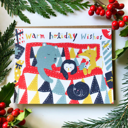 Colorful holiday greeting card featuring cartoon animals surrounded by festive elements, pine branches, and red berries, with "Warm holiday wishes" text on top