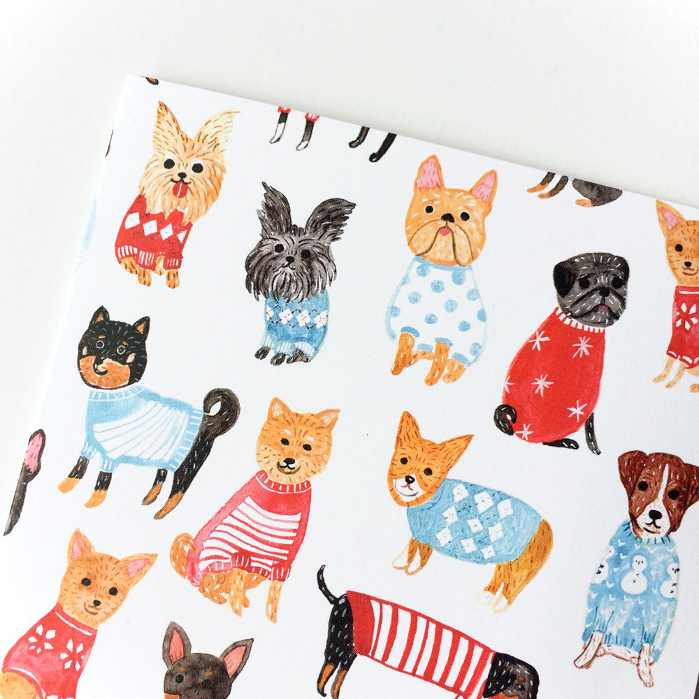 Holiday greeting card featuring colorful illustrations of various small dog breeds wearing festive sweaters and outfits, arranged in a playful pattern on a white background