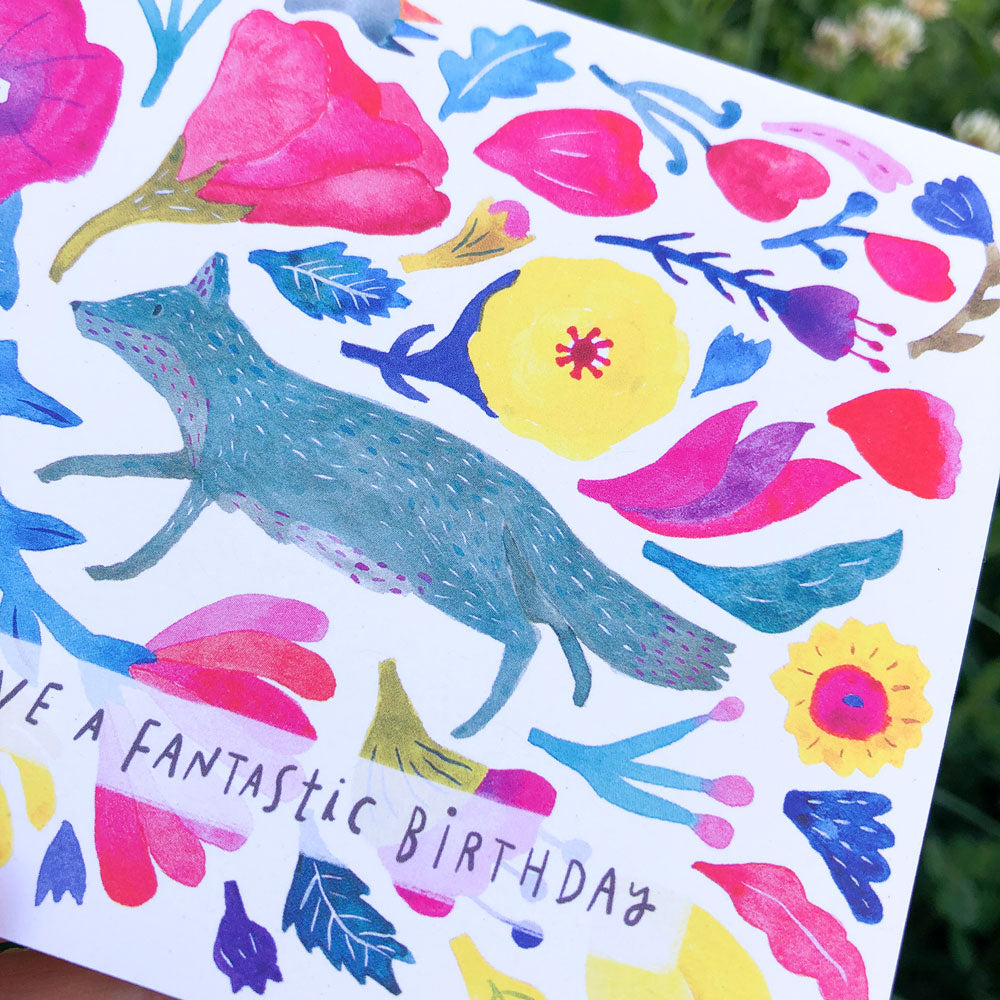 Colorful watercolor birthday card featuring a blue fox surrounded by vibrant flowers and leaves, with text reading 'Have a Fantastic Birthday' on white recycled card stock