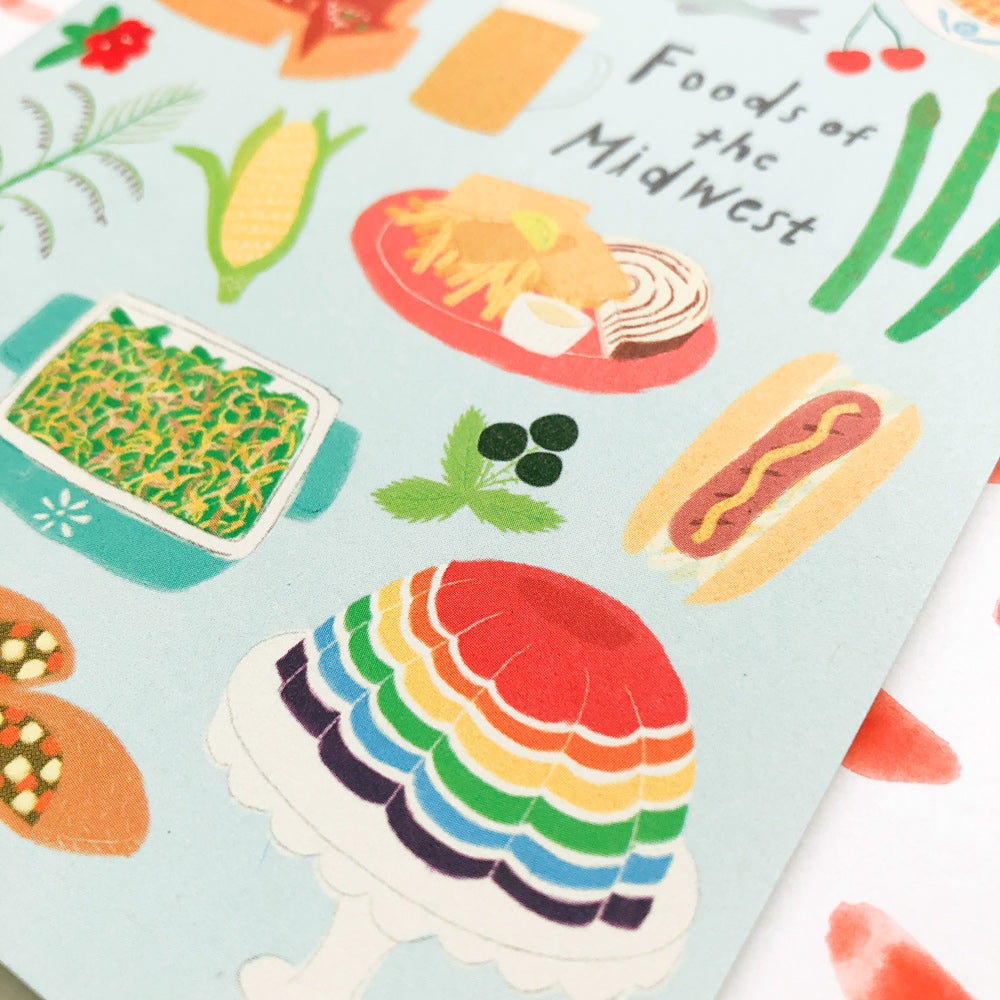 Colorful illustration of Midwest foods including corn, hot dog, casserole, rainbow jello, and cherry on light blue background with "Foods of the Midwest" text, showcasing regional cuisine on a greeting card