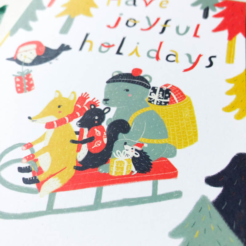 Colorful illustration of woodland animals on a sleigh with holiday text, surrounded by festive trees and presents, perfect for a cheerful greeting card design