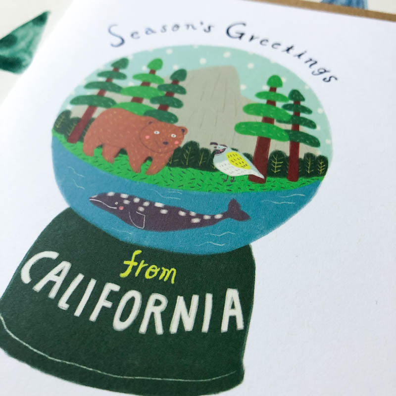 Snow globe greeting card featuring California wildlife: bear, seagull, and whale in a scenic forest and ocean setting, with "Season's Greetings from California" text