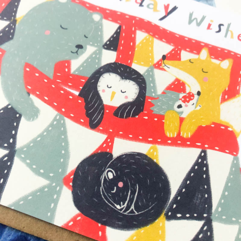 Cute holiday greeting card featuring cartoon animals including a penguin, bear, cat, and rabbit, wrapped in a festive red scarf with geometric shapes in the background and "Holiday Wishes" text at the top
