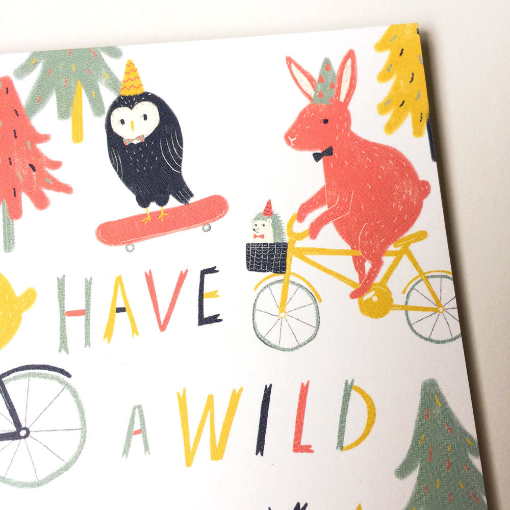 Colorful birthday card featuring whimsical woodland animals, including an owl on a skateboard and a rabbit riding a bicycle, with text "Have a Wild" in playful lettering against a white background with stylized trees.