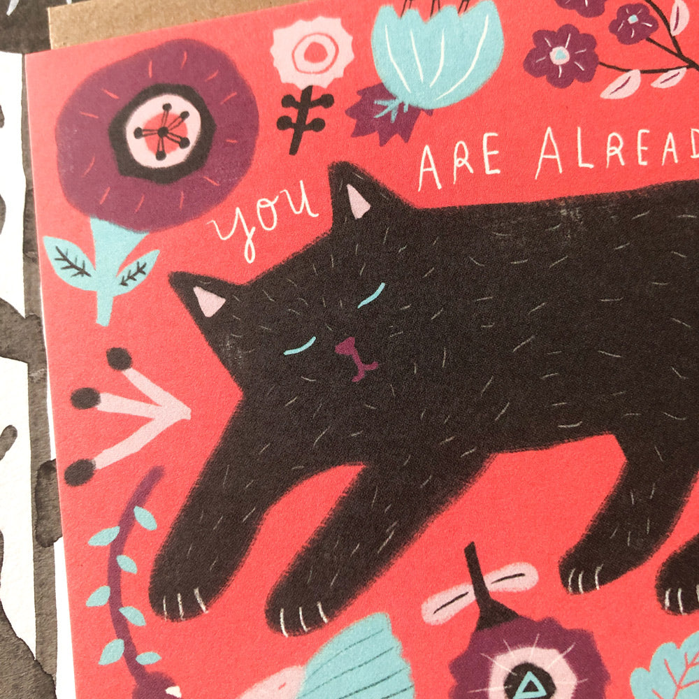 Colorful greeting card featuring a black cat illustration surrounded by floral designs on a coral background, with partial text "you are alrea" visible