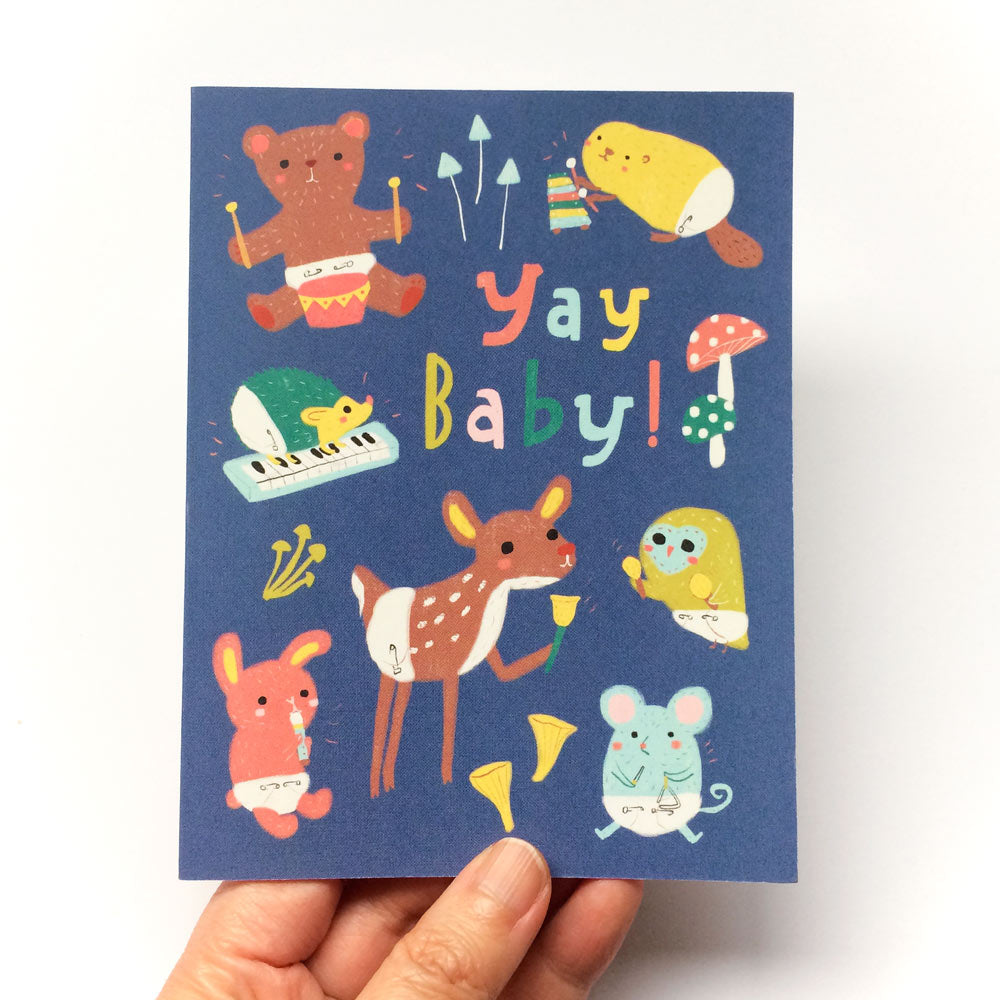 Colorful baby animal greeting card featuring woodland creatures in diapers playing instruments, with "Yay Baby!" text on a navy background. Includes bear, bird, deer, mouse, and other cute animals in whimsical illustrated style.