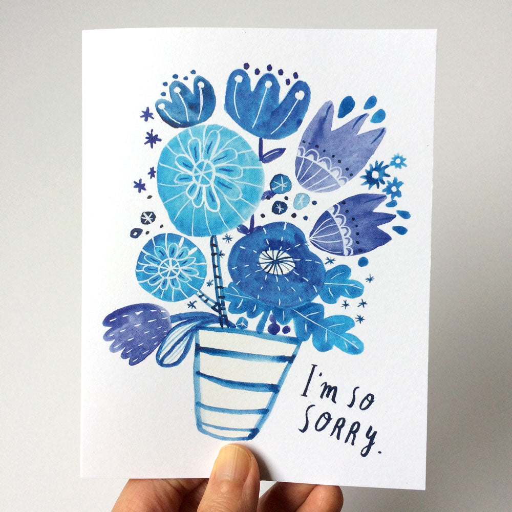 Watercolor sympathy card featuring blue floral bouquet in striped vase with handwritten text "I'm so sorry" on white background, held by hand