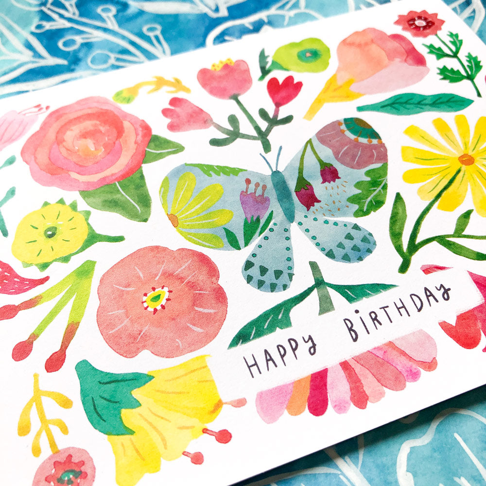 Colorful watercolor birthday card featuring a vibrant butterfly, flowers, and "Happy Birthday" text amidst a whimsical floral arrangement on white recycled card stock