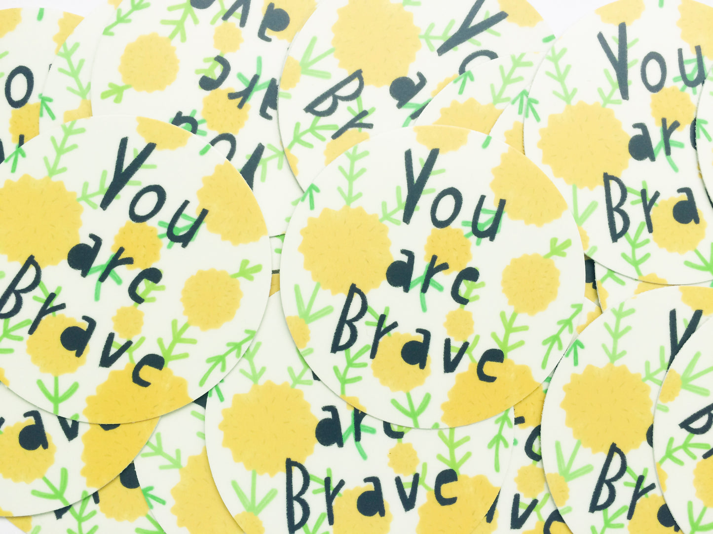 Colorful pattern of yellow circles with 'You are Brave' text repeated, interspersed with green leaf-like designs on a white background, showcasing a motivational vinyl sticker design