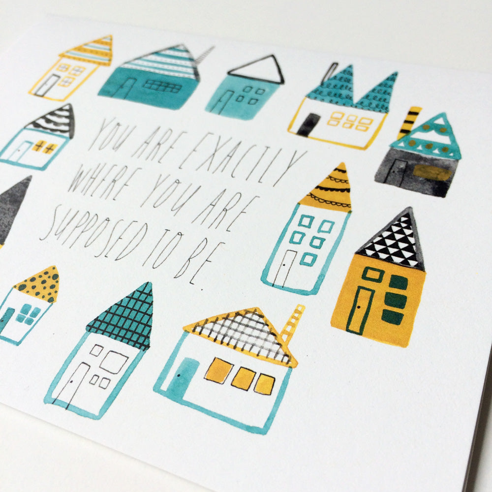 Colorful hand-drawn houses surrounding inspirational text "You are exactly where you are supposed to be" on white greeting card, featuring teal, yellow, and black geometric designs