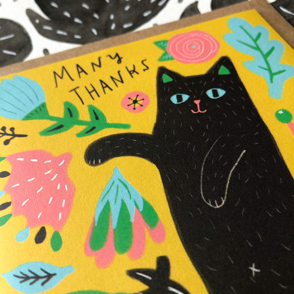 Colorful greeting card featuring a black cat surrounded by floral designs on a yellow background, with "Many Thanks" text, perfect for expressing gratitude with a whimsical feline touch