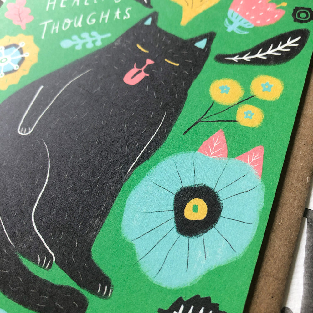 Colorful sympathy card featuring a black cat with pink tongue surrounded by whimsical flowers and leaves on green background, with 'Healing Thoughts' text visible