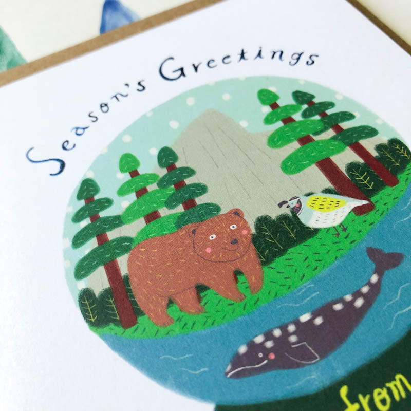 Charming holiday greeting card featuring a snow globe scene with Northern California wildlife including a bear, whale, and bird among pine trees and water, with 'Season's Greetings' text