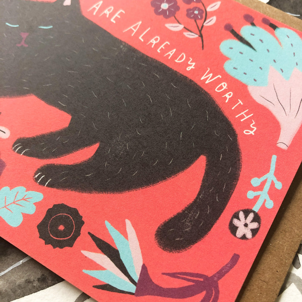 Colorful greeting card featuring a black cat silhouette on a coral background with blue and white floral elements, and text reading "You are already worthy