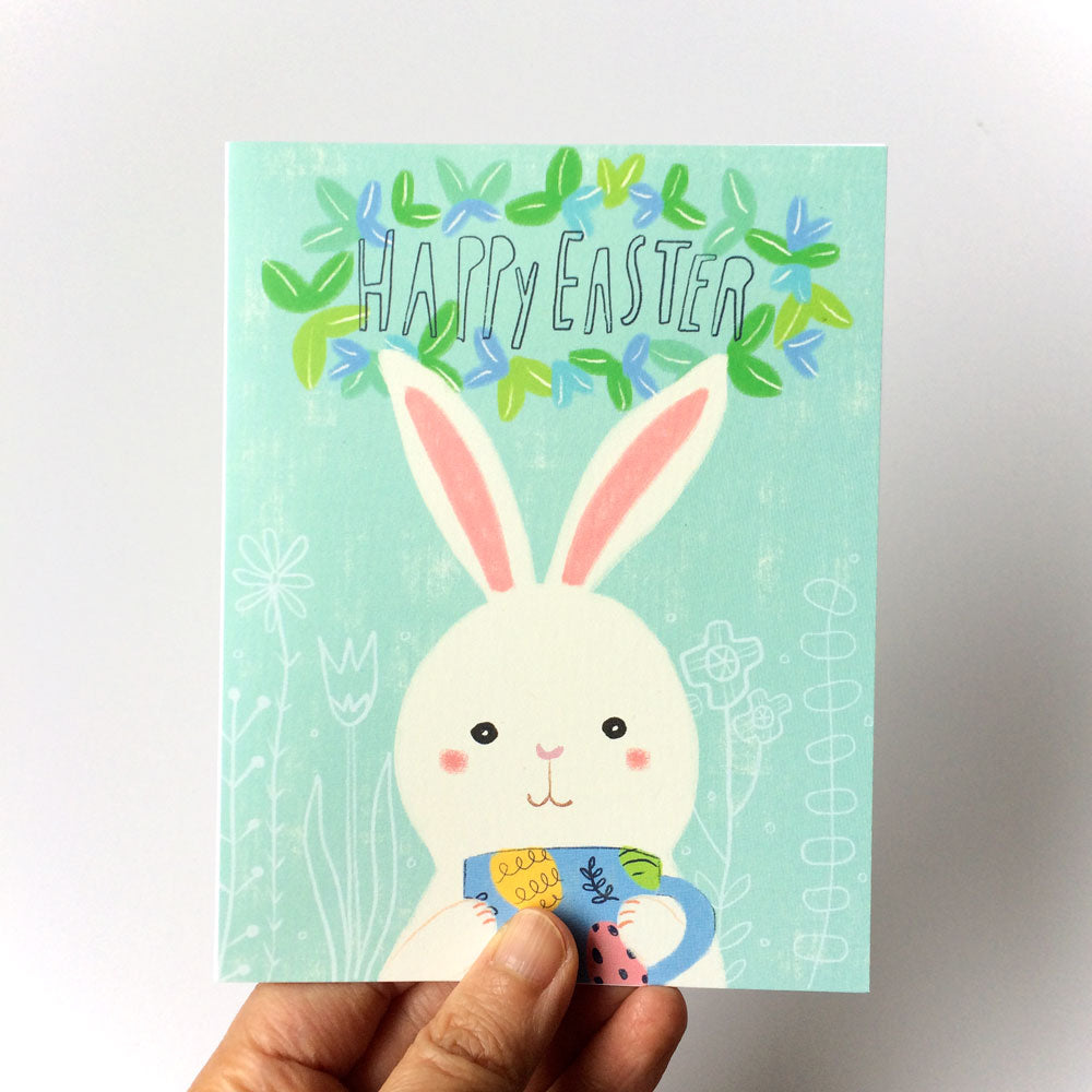 Cute Easter greeting card featuring a white bunny holding a colorful mug, with "Happy Easter" text and floral design on mint green background