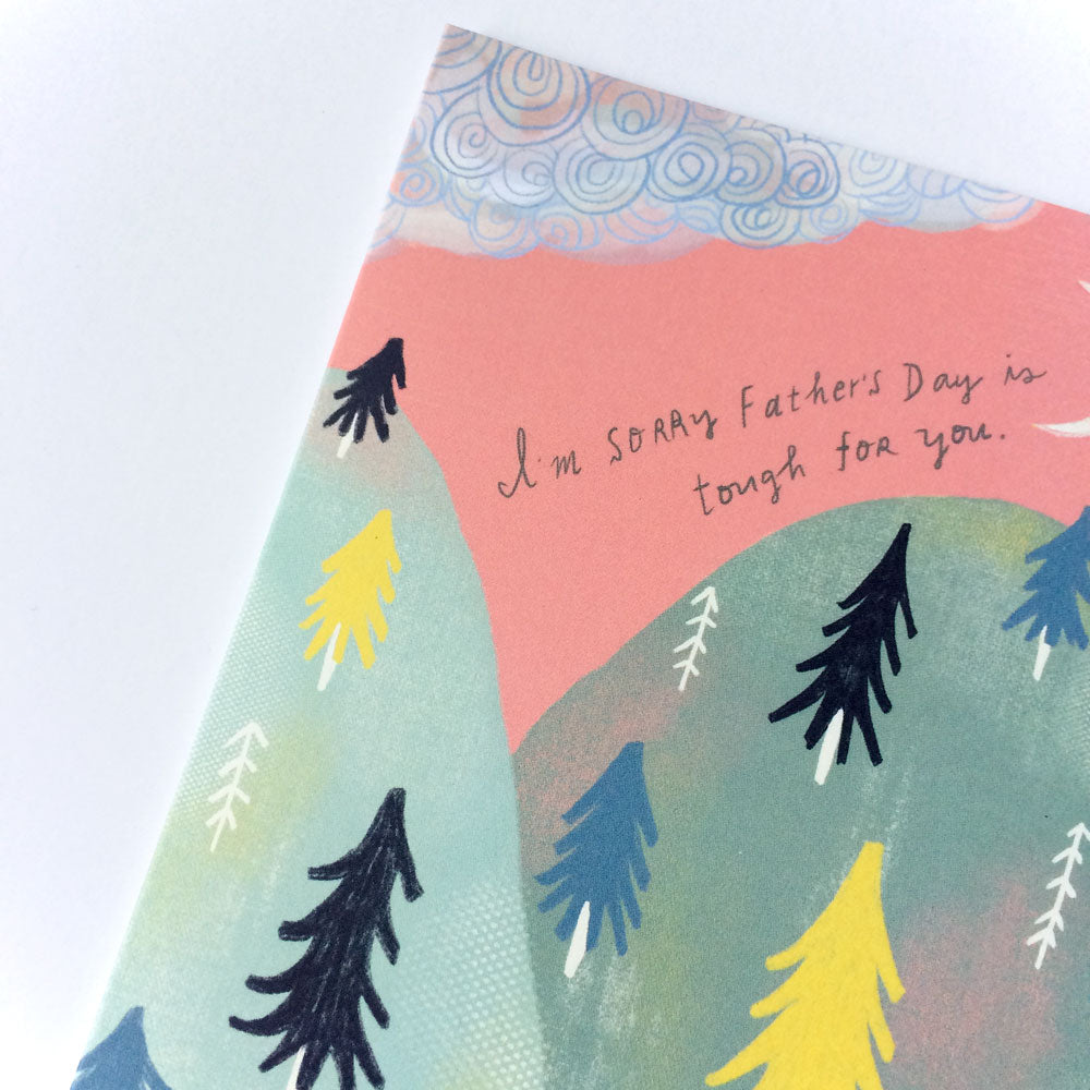 Empathy card featuring pastel mountains with pine trees, swirly clouds, and handwritten text "I'm sorry Father's Day is tough for you" on pink sky background