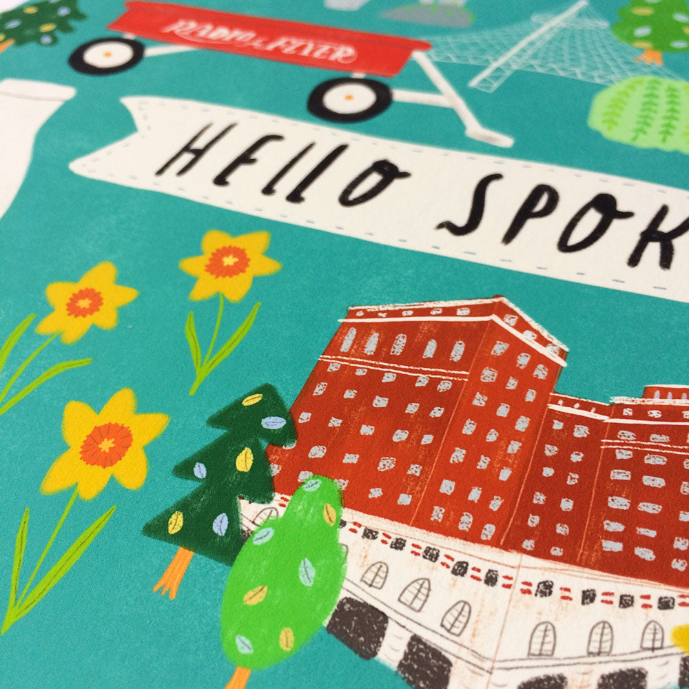 Colorful illustration of Spokane landmarks featuring "Hello Spokane" text, red wagon, historic building, yellow flowers, and green trees on teal background, showcasing city's charm and attractions