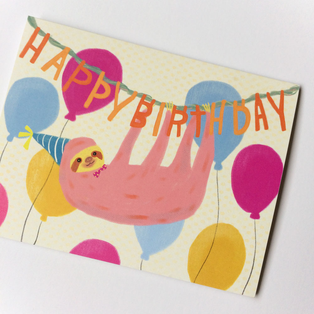 Colorful birthday card featuring a cute pink sloth wearing a party hat, hanging from "Happy Birthday" text surrounded by festive balloons in yellow, blue, and magenta on a cream background