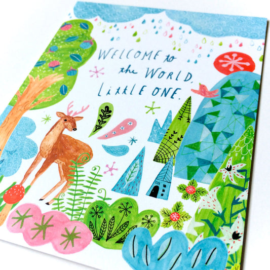 Colorful baby greeting card featuring whimsical forest scene with deer, trees, flowers, and "Welcome to the World Little One" hand-lettered text. Vibrant watercolor-style illustration on white background.