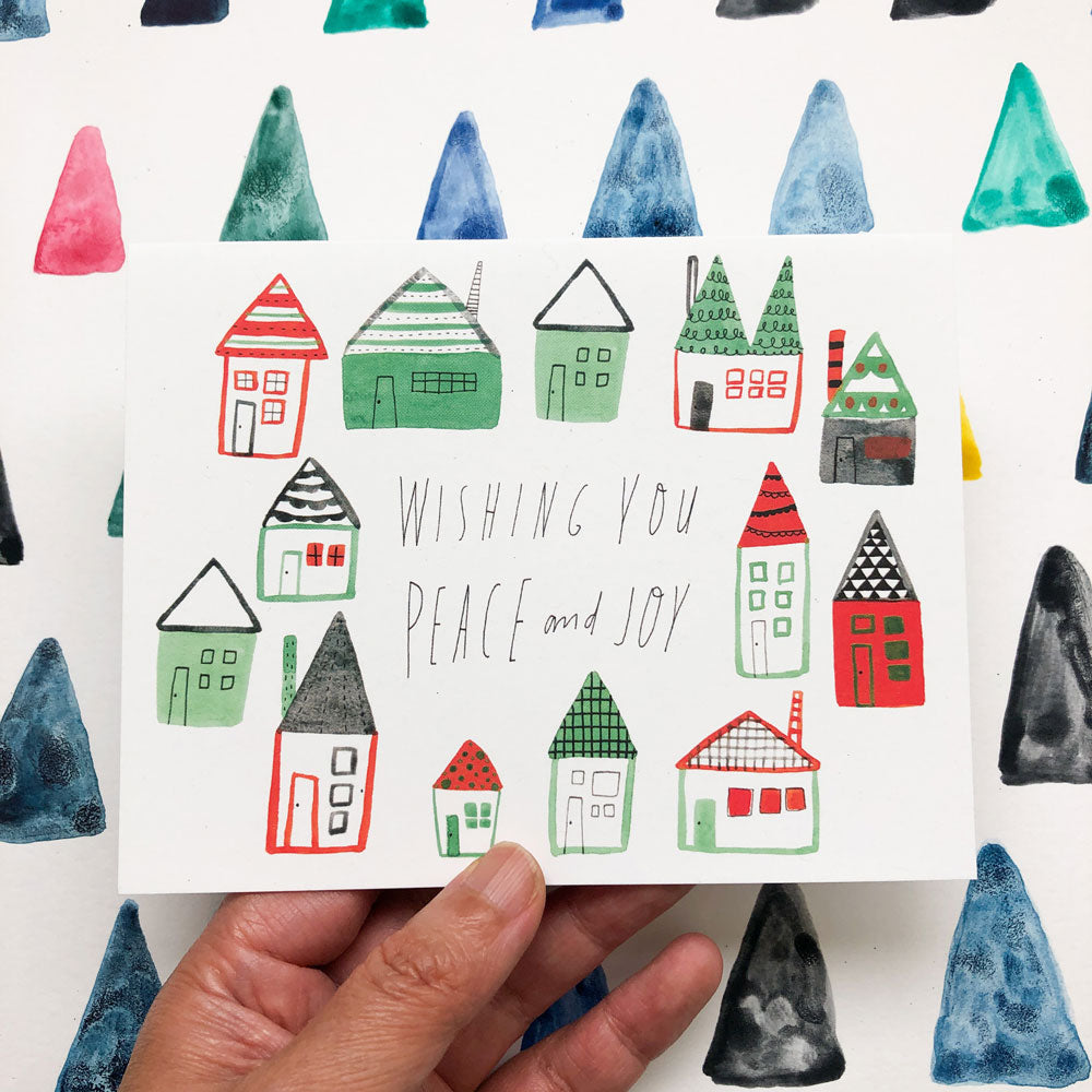 Watercolor holiday greeting card featuring whimsical hand-drawn houses in green and red, with "Wishing You Peace and Joy" handwritten message, surrounded by colorful abstract triangles