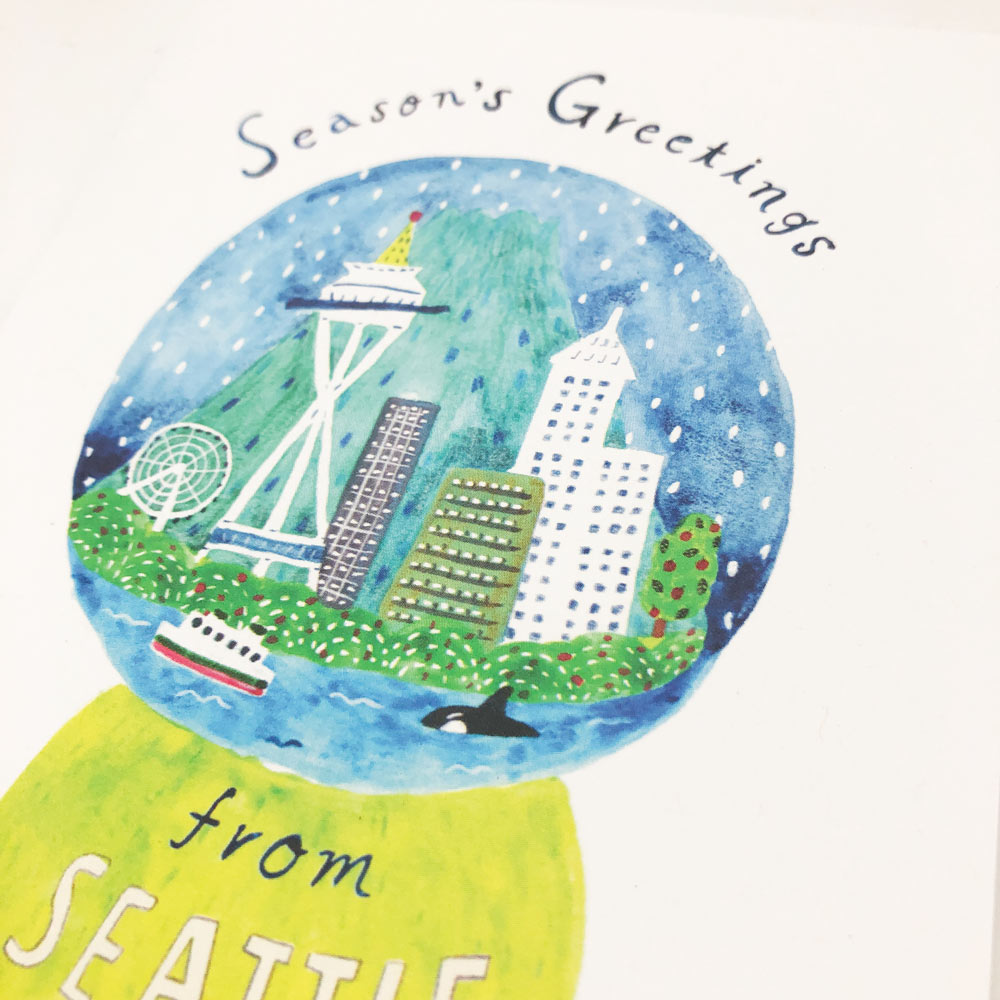 Watercolor greeting card featuring Seattle skyline in a snow globe, with Space Needle, buildings, ferry, and orca. Text reads "Season's Greetings from Seattle" in a festive, holiday-themed design.
