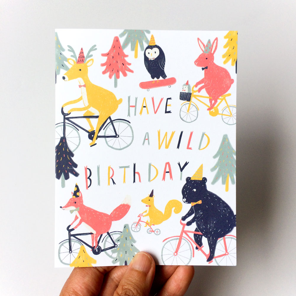 Colorful birthday card featuring whimsical woodland animals riding bicycles and skateboard among trees, with text "Have a wild birthday" in vibrant letters