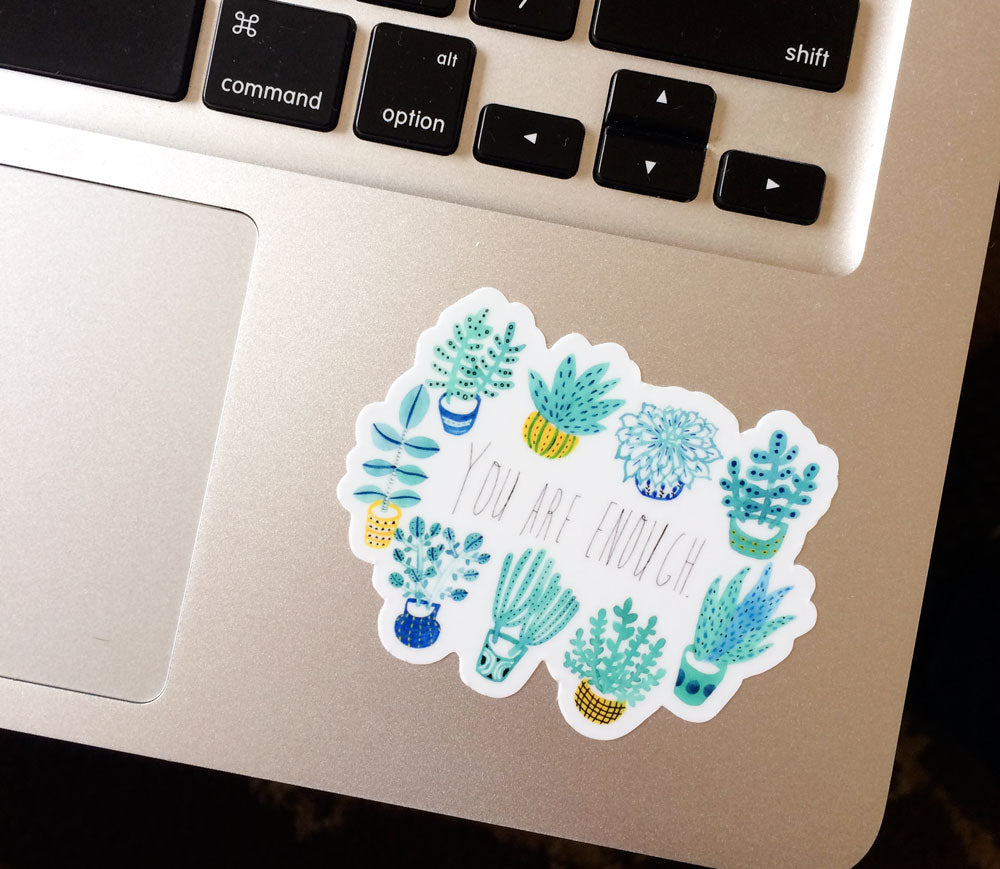 Vinyl sticker with "You Are Enough" text surrounded by colorful succulent plant illustrations, placed on a laptop keyboard