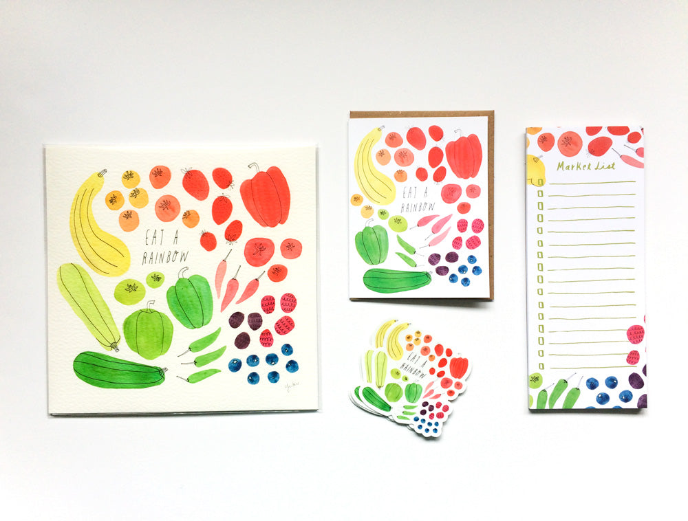 Colorful fruit and vegetable illustrations on various products including a canvas print, greeting card, sticker, and notepad, arranged on a white background to showcase the "Eat a Rainbow" design concept