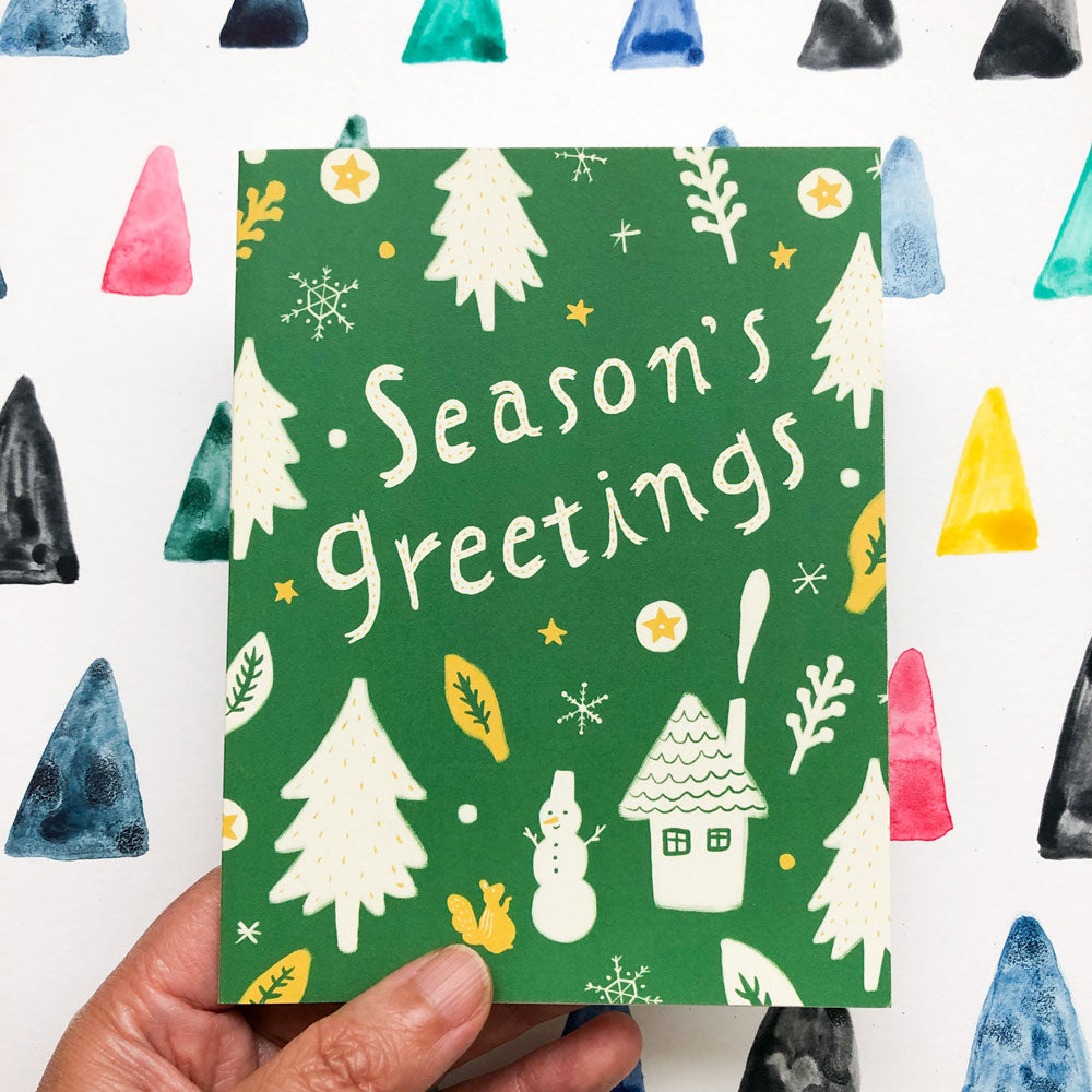 Festive green holiday card with "Season's Greetings" text, featuring white Christmas trees, snowflakes, a snowman, house, and golden stars, surrounded by colorful triangular shapes