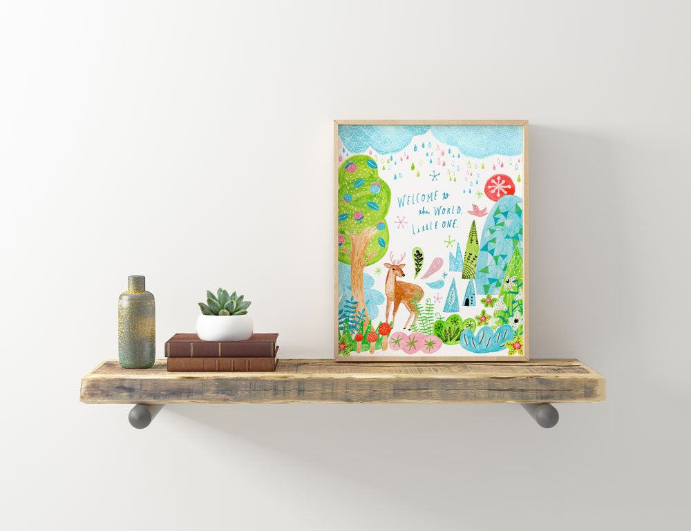 Framed watercolor woodland nursery art print featuring deer and colorful forest, displayed on rustic wooden shelf with decor items