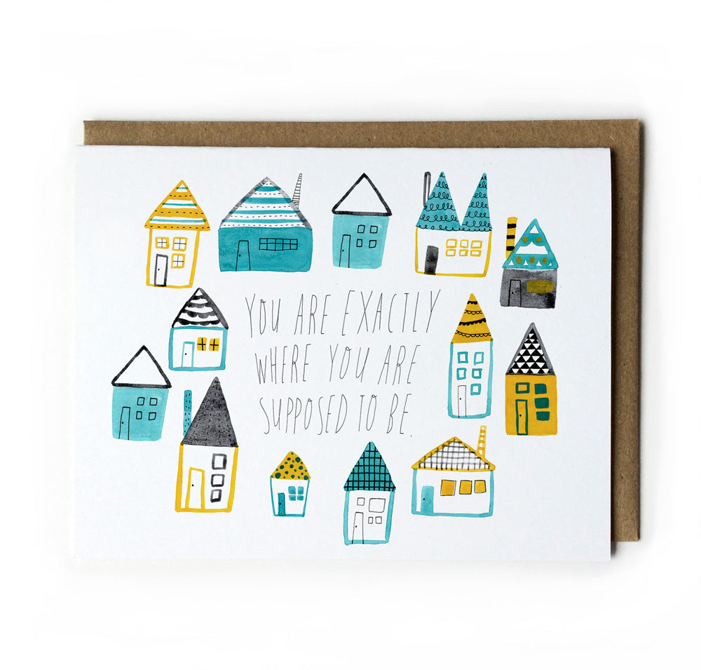 Greeting card with colorful hand-drawn houses surrounding text "You are exactly where you are supposed to be" on white background, paired with kraft paper envelope