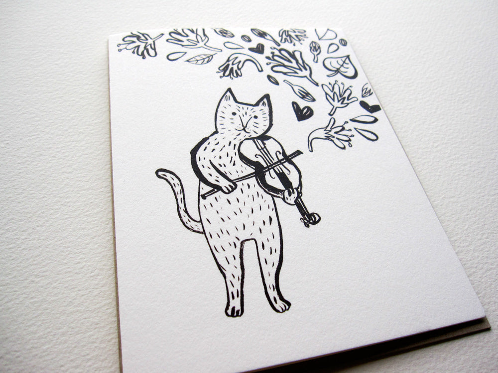 Black and white greeting card featuring a whimsical illustration of a cat playing violin, surrounded by floral elements and hearts. Simple line drawing style on recycled white card stock, perfect for cat lovers or as a unique Valentine's Day card.
