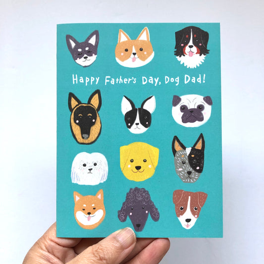 Teal Father's Day card featuring diverse dog breed faces with text "Happy Father's Day, Dog Dad!" Includes various breeds like Husky, Corgi, Bernese Mountain Dog, German Shepherd, Boston Terrier, Pug, and more. Hand holding the card visible.