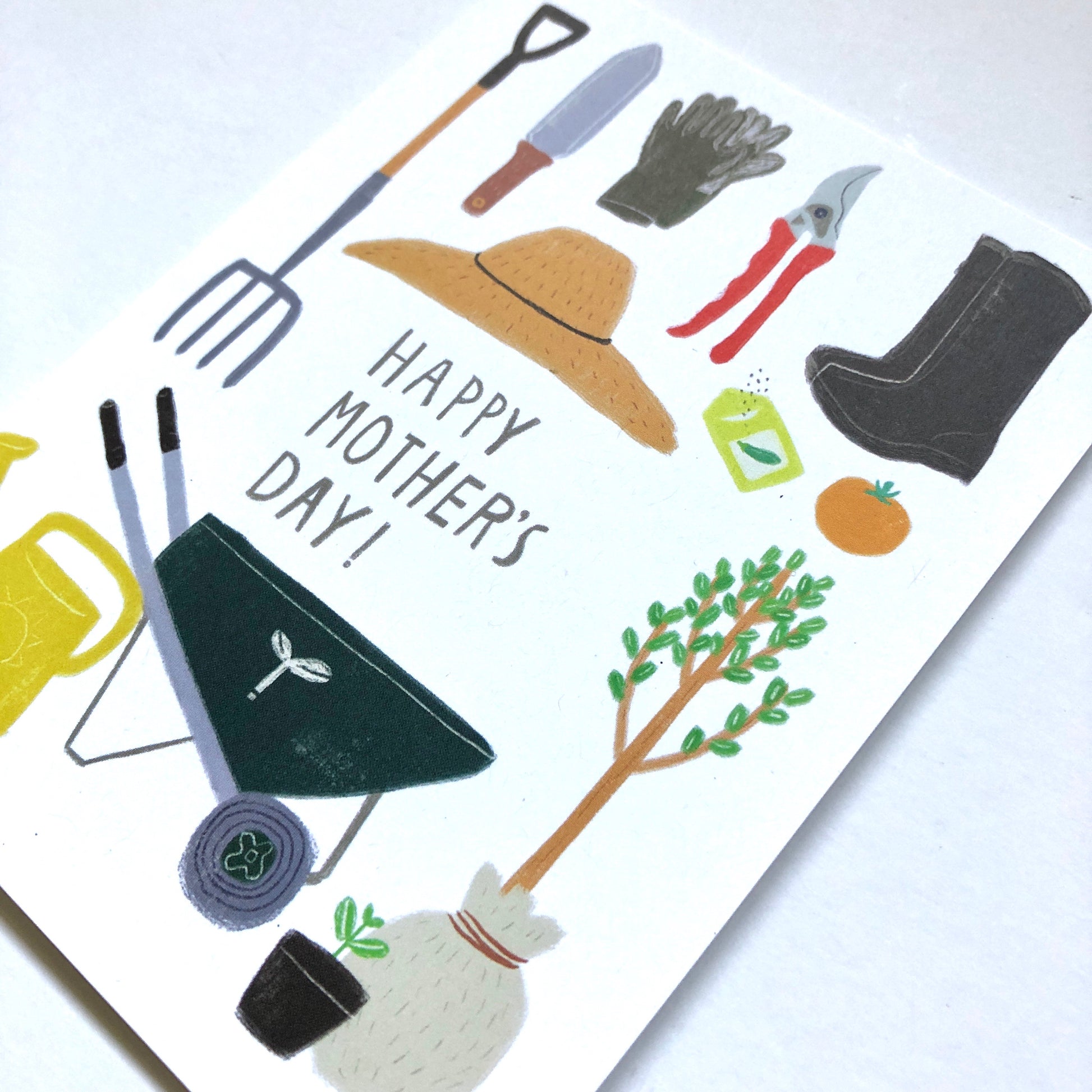 Mother's Day card featuring colorful gardening tools and elements including a pitchfork, trowel, gloves, hat, pruning shears, boots, watering can, wheelbarrow, seedling, and potted plant, with "Happy Mother's Day!" text in the center