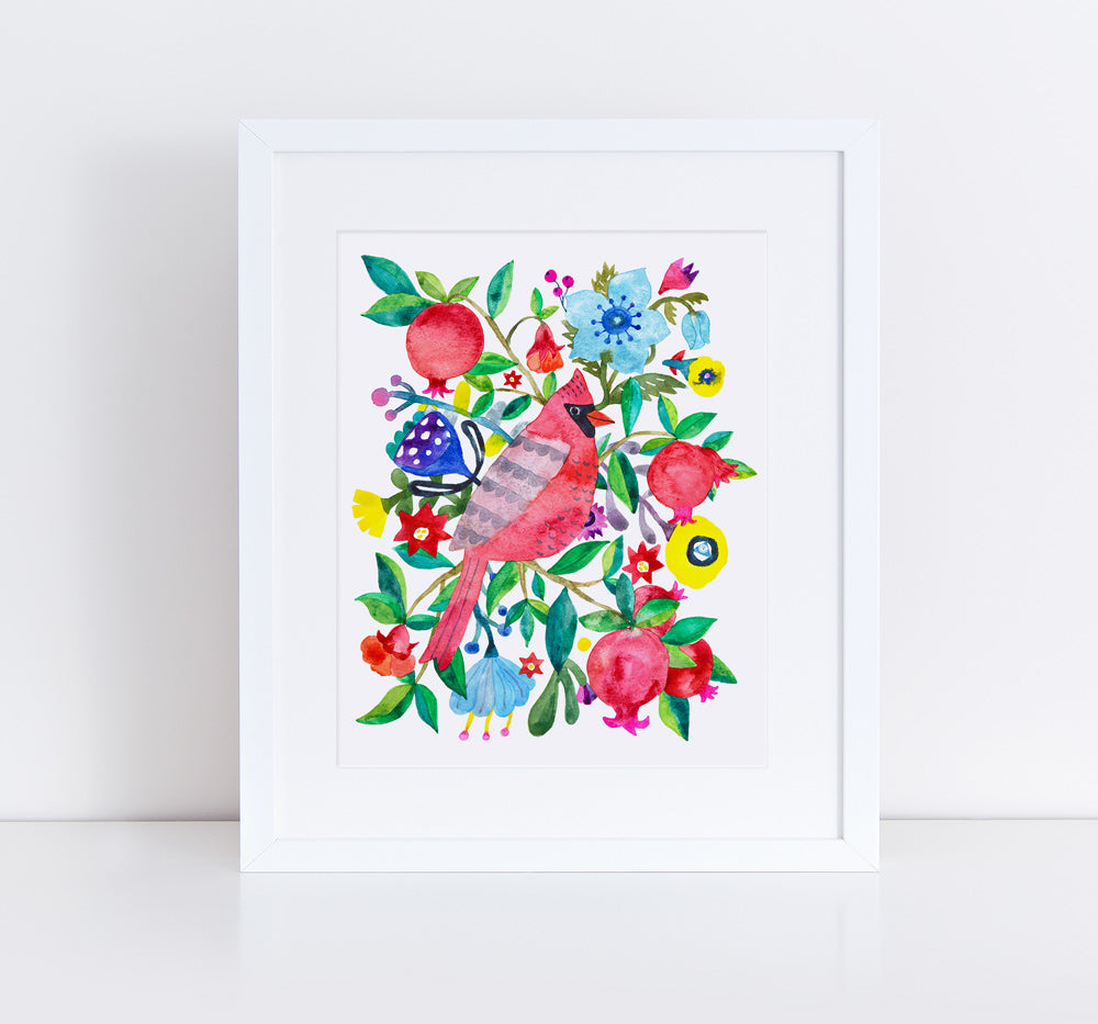 Colorful watercolor art print featuring a red cardinal bird surrounded by vibrant flowers, pomegranates, and foliage in a white frame against a light background, showcasing a whimsical and lively garden scene