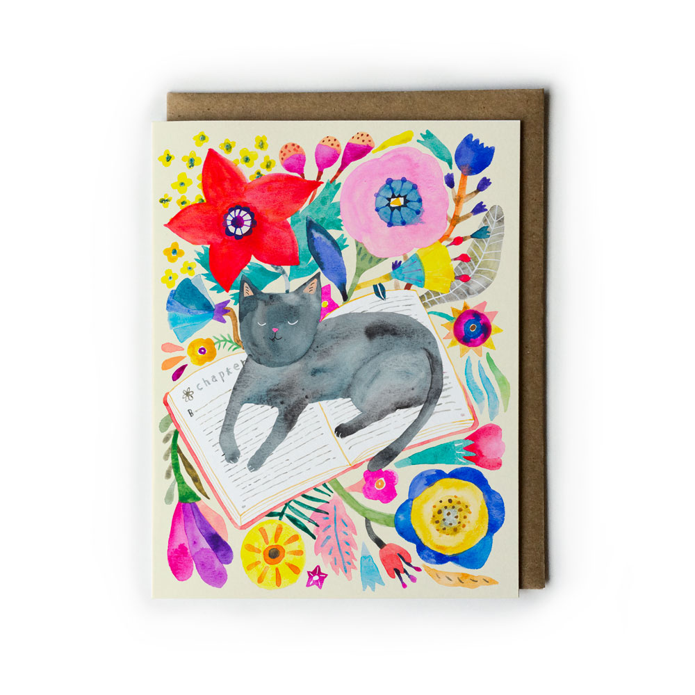 Colorful watercolor greeting card featuring a gray cat napping on an open book, surrounded by vibrant flowers and foliage in various hues, with a kraft paper envelope