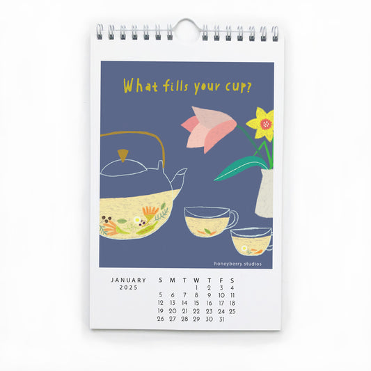 2025 wall calendar page for January featuring colorful illustration of teapot, cups, and flowers on blue background with inspirational text "What fills your cup?" and monthly date grid