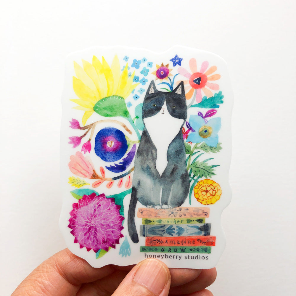 Colorful watercolor sticker featuring a tuxedo cat sitting on books, surrounded by vibrant flowers and foliage, perfect for cat lovers and book enthusiasts