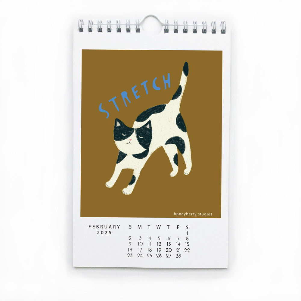 2025 wall calendar page for February featuring a playful illustration of a stretching black and white cat on a golden background, with "STRETCH" text above and date grid below