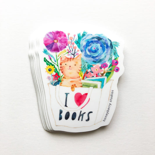 Watercolor sticker of orange tabby cat peeking out of a white book bag with "I love books" text, surrounded by colorful flowers and foliage