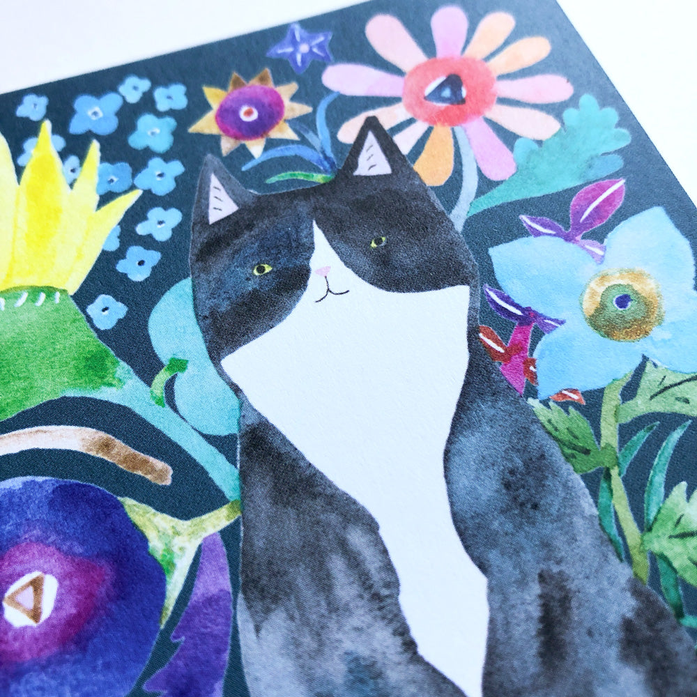 Colorful watercolor greeting card featuring a tuxedo cat surrounded by vibrant flowers, stars, and whimsical shapes on a dark background. The cat's expressive face and white chest contrast with its black fur and the lively floral design.