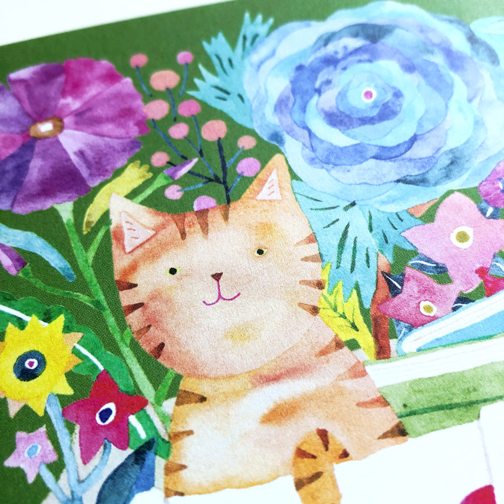 Watercolor illustration of an orange tabby cat peeking out from a book bag surrounded by colorful flowers including a purple bloom, blue rose, and yellow sunflower on a green background