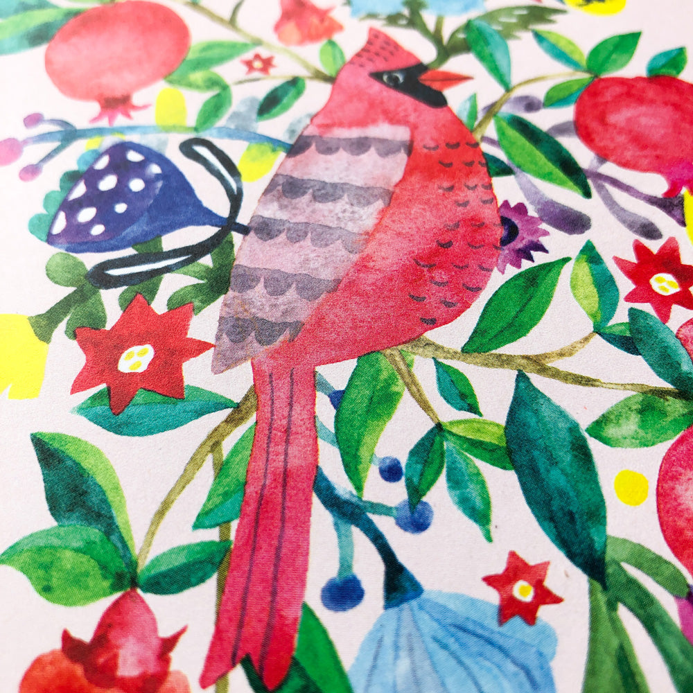 Watercolor illustration of a vibrant red cardinal perched among colorful pomegranates, flowers, and foliage, creating a festive holiday scene with bright reds, greens, and blues on a white background.