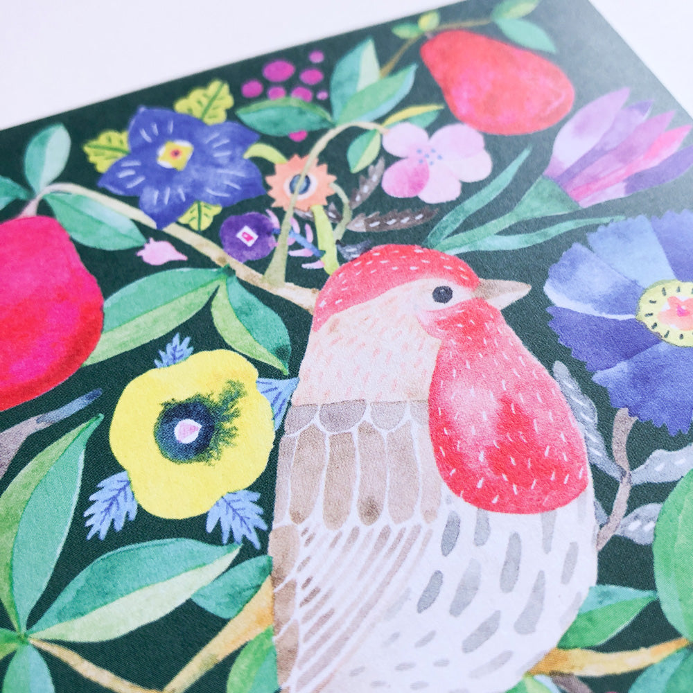 Vibrant watercolor illustration of a red house finch surrounded by colorful flowers, leaves, and red pears on a dark background. Close-up view of greeting card featuring festive holiday-themed artwork with rich, bold colors and whimsical botanical elements.