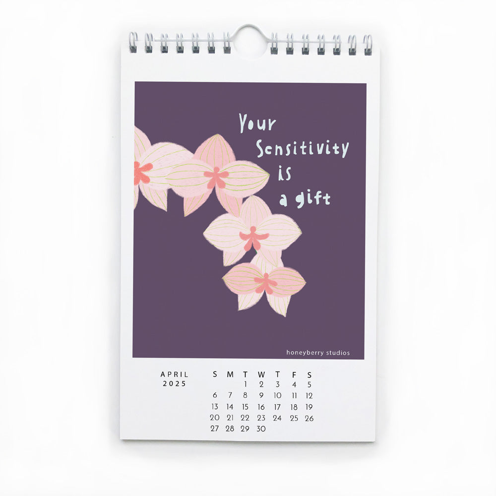 2025 Follow Your Joy wall calendar page for April featuring pink orchids and inspirational quote "Your Sensitivity is a gift" on purple background, with monthly date grid below