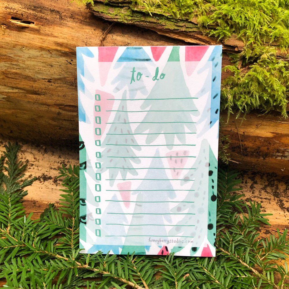 Christmas Forest To-Do List notepad with colorful watercolor tree illustrations, displayed on natural wood and moss background, perfect for holiday organization and nature lovers